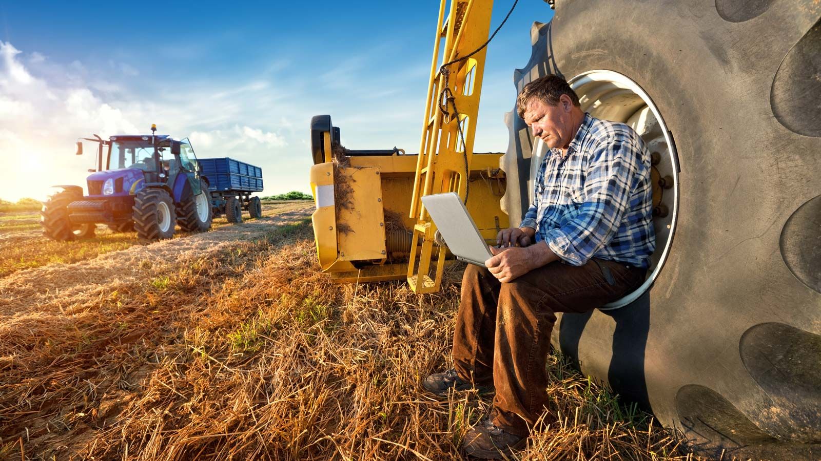 Farmer working on a computer sitting on the tire of his machine